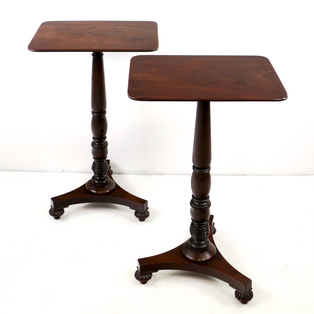 A pair of mahogany Regency wine tables featuring rounded rectangular tops, central turned pedestal columns, and tri-form bases resting on carved feet.