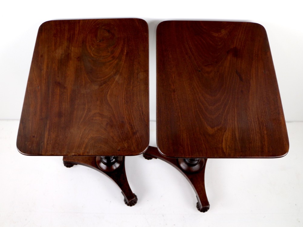 A pair of mahogany Regency wine tables featuring rounded rectangular tops, central turned pedestal columns, and tri-form bases resting on carved feet. View X
