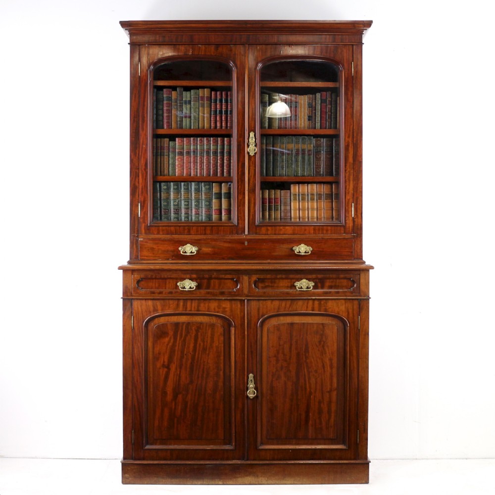 An early Victorian mahogany bookcase featuring an upper glazed section with two arched doors and a lower cupboard base with two drawers.