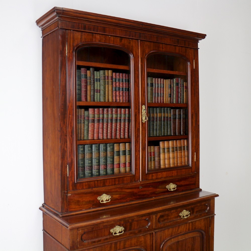 An early Victorian mahogany bookcase featuring an upper glazed section with two arched doors and a lower cupboard base with two drawers. View V