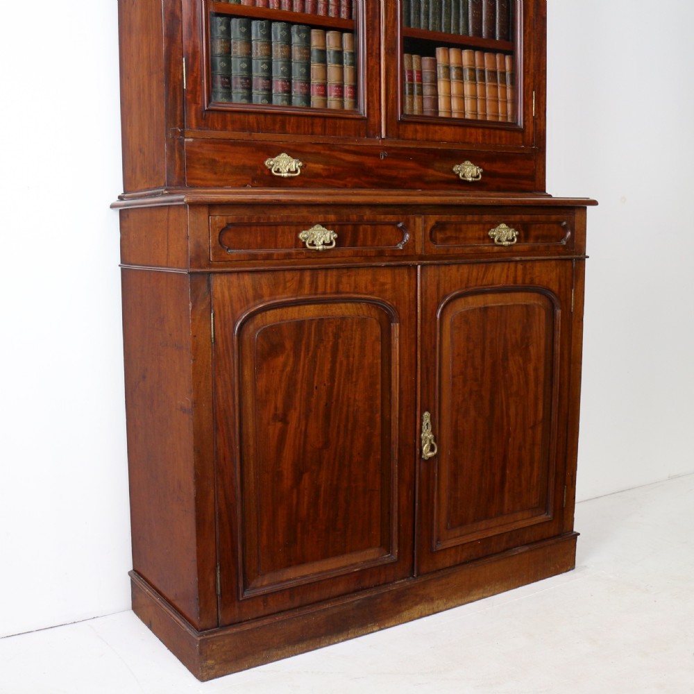 An early Victorian mahogany bookcase featuring an upper glazed section with two arched doors and a lower cupboard base with two drawers. View VI