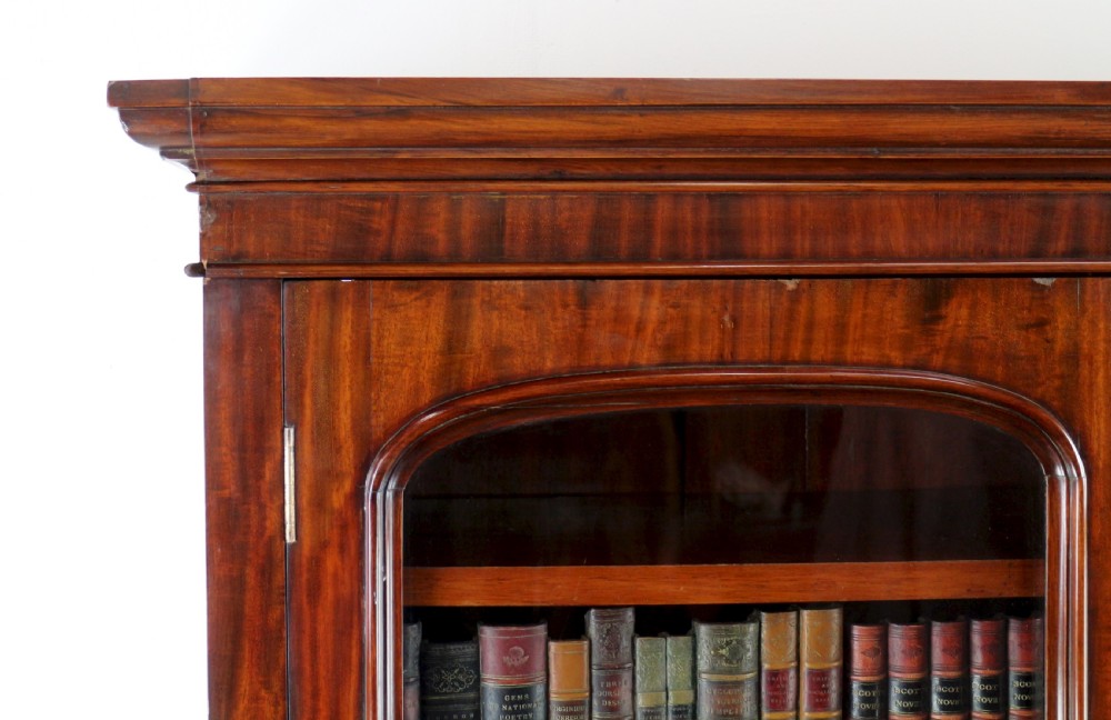 An early Victorian mahogany bookcase featuring an upper glazed section with two arched doors and a lower cupboard base with two drawers. View IX