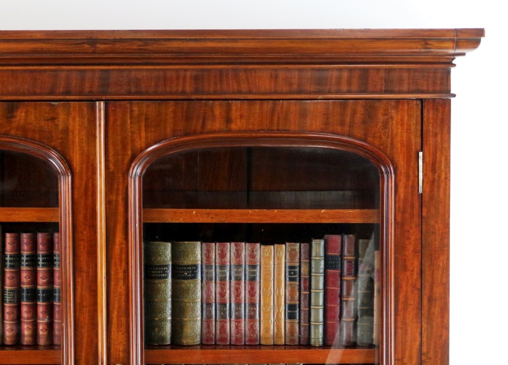 An early Victorian mahogany bookcase featuring an upper glazed section with two arched doors and a lower cupboard base with two drawers. View X