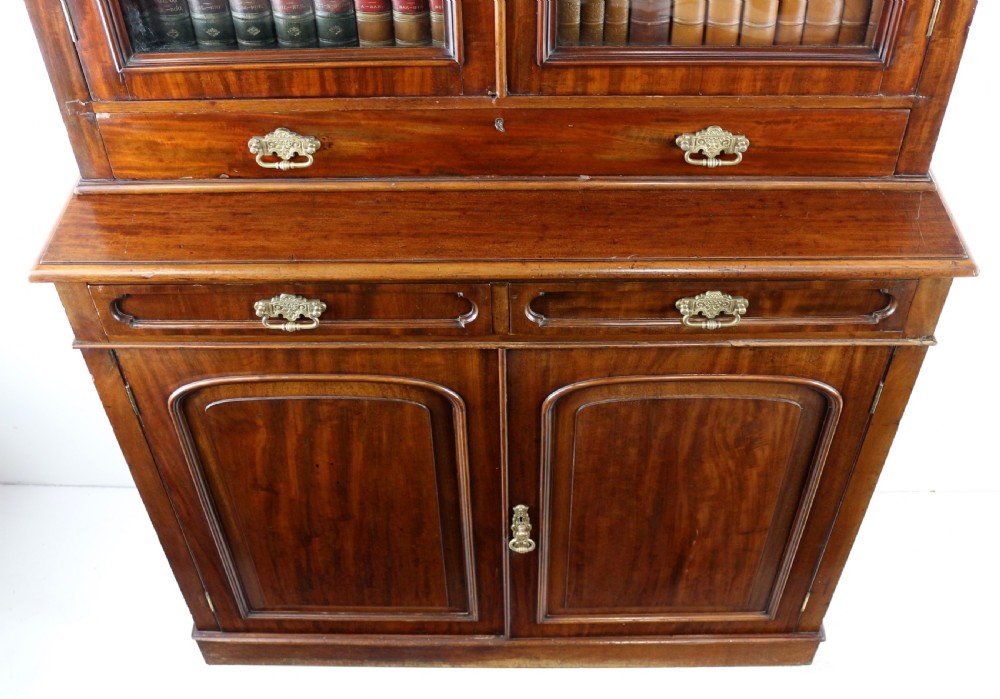 An early Victorian mahogany bookcase featuring an upper glazed section with two arched doors and a lower cupboard base with two drawers. View XX