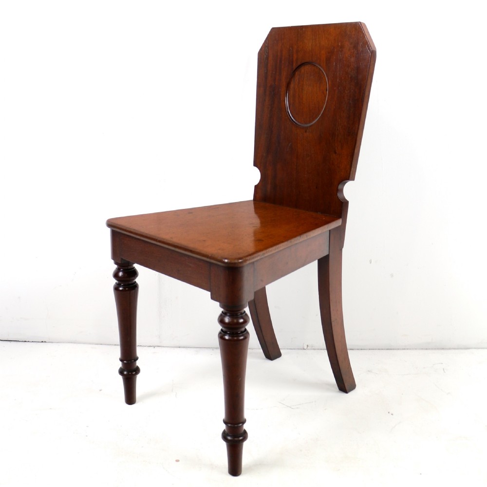 A set of four Victorian mahogany hall chairs featuring shaped solid wooden backs with recessed circular central details, flat wooden seats, turned front legs, and flared rear legs. View VIII