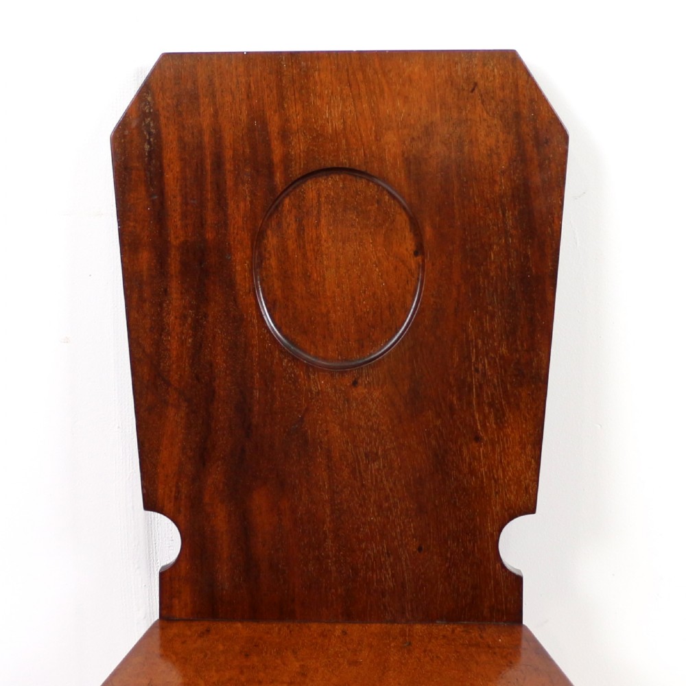 A set of four Victorian mahogany hall chairs featuring shaped solid wooden backs with recessed circular central details, flat wooden seats, turned front legs, and flared rear legs. View IX