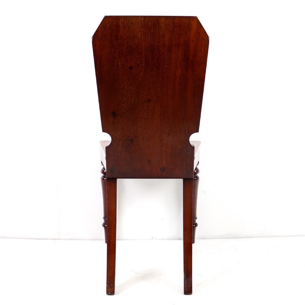 A set of four Victorian mahogany hall chairs featuring shaped solid wooden backs with recessed circular central details, flat wooden seats, turned front legs, and flared rear legs. View XI
