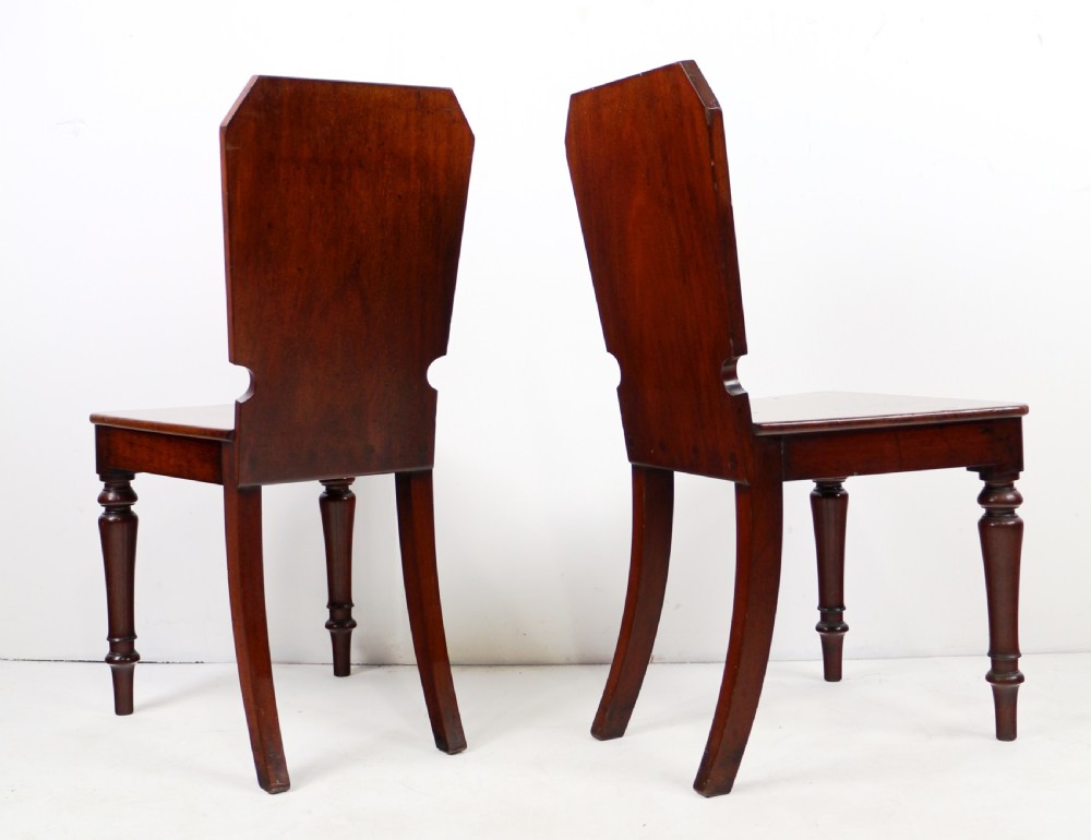 A set of four Victorian mahogany hall chairs featuring shaped solid wooden backs with recessed circular central details, flat wooden seats, turned front legs, and flared rear legs. View XVII