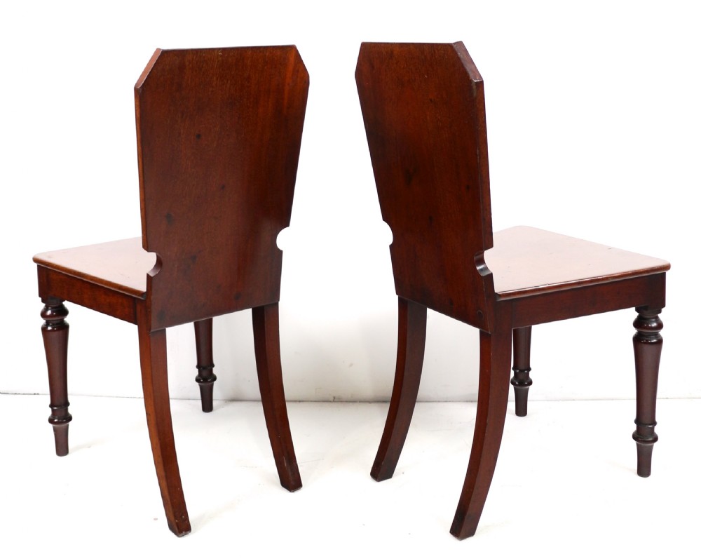 A set of four Victorian mahogany hall chairs featuring shaped solid wooden backs with recessed circular central details, flat wooden seats, turned front legs, and flared rear legs. View XXI