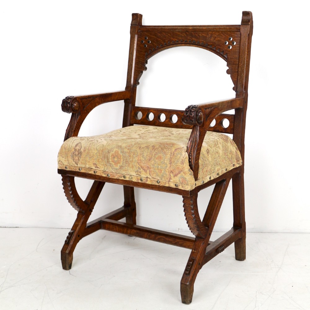 A Gothic Revival carved dark oak armchair featuring an arched backrest with quatrefoil cutouts, curved legs, and a patterned fabric seat.