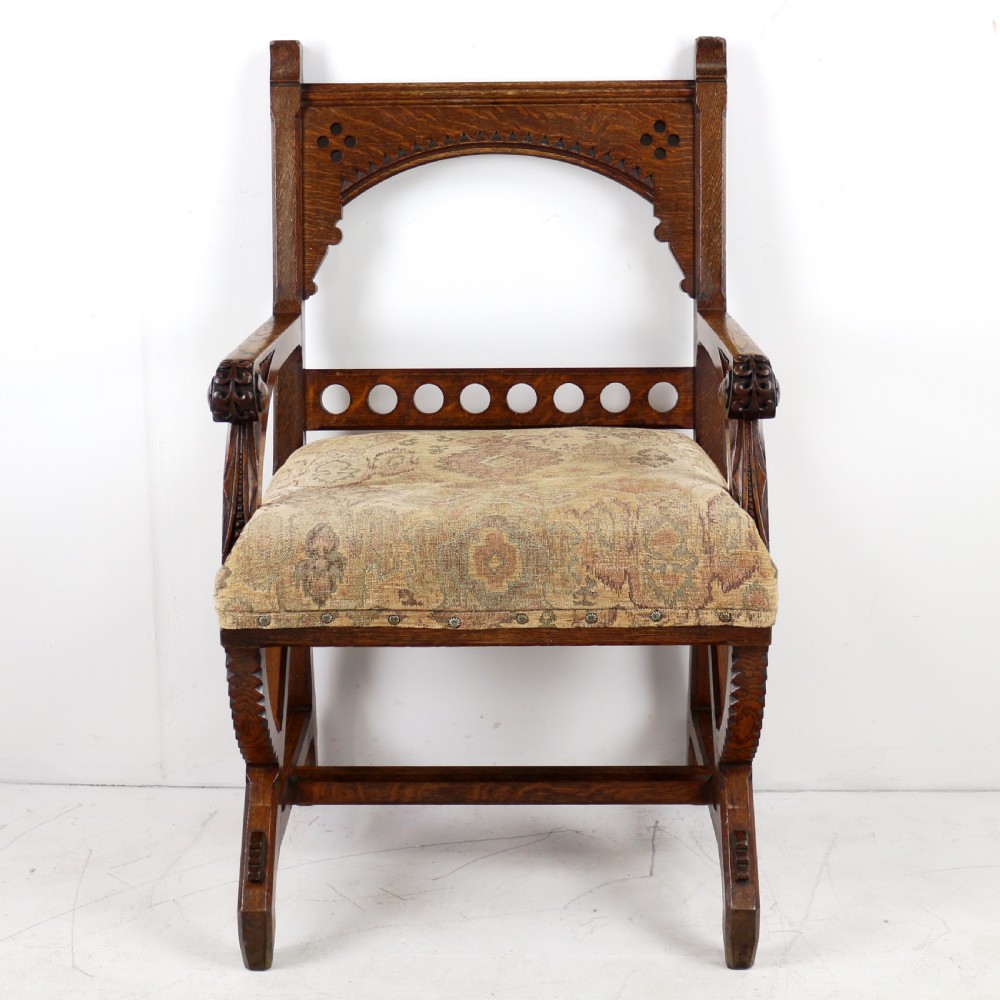 A Gothic Revival carved dark oak armchair featuring an arched backrest with quatrefoil cutouts, curved legs, and a patterned fabric seat. View II