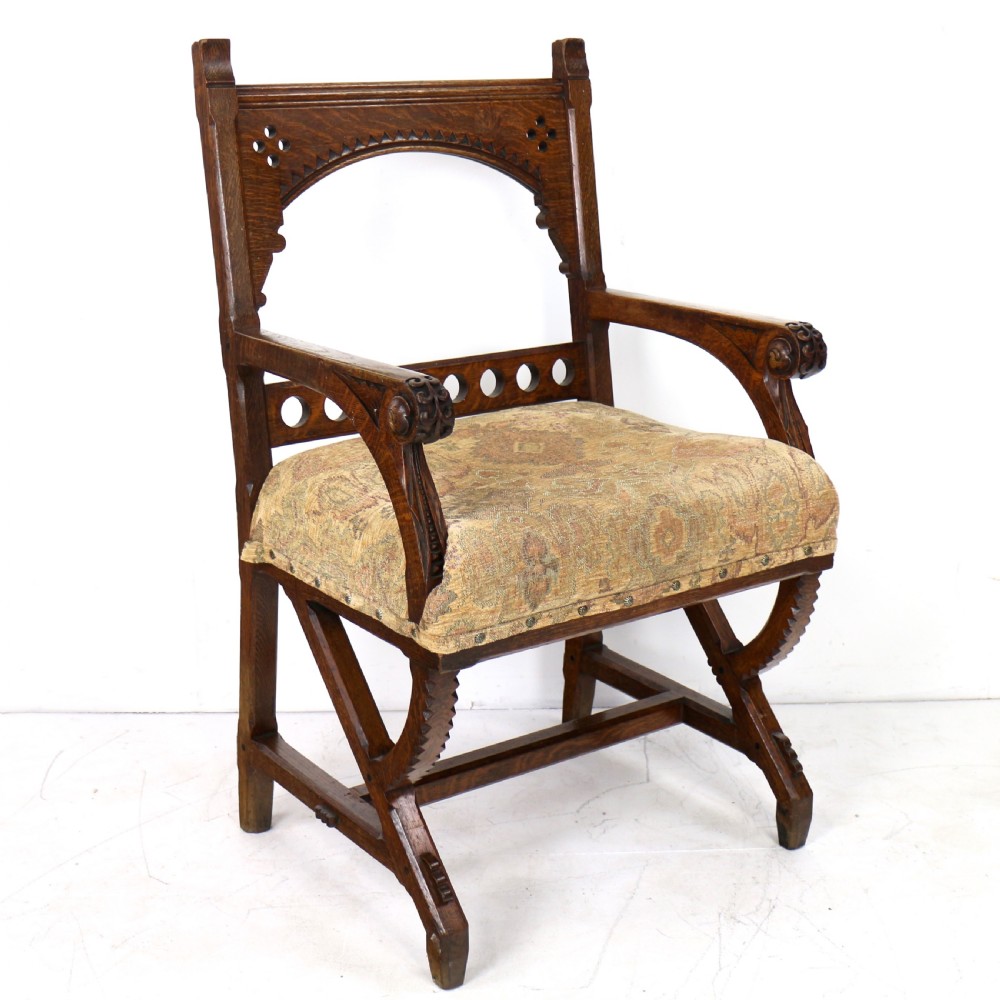 A Gothic Revival carved dark oak armchair featuring an arched backrest with quatrefoil cutouts, curved legs, and a patterned fabric seat. View III