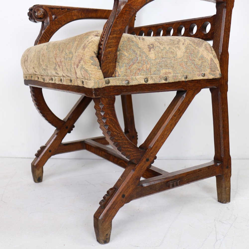 A Gothic Revival carved dark oak armchair featuring an arched backrest with quatrefoil cutouts, curved legs, and a patterned fabric seat. View VI