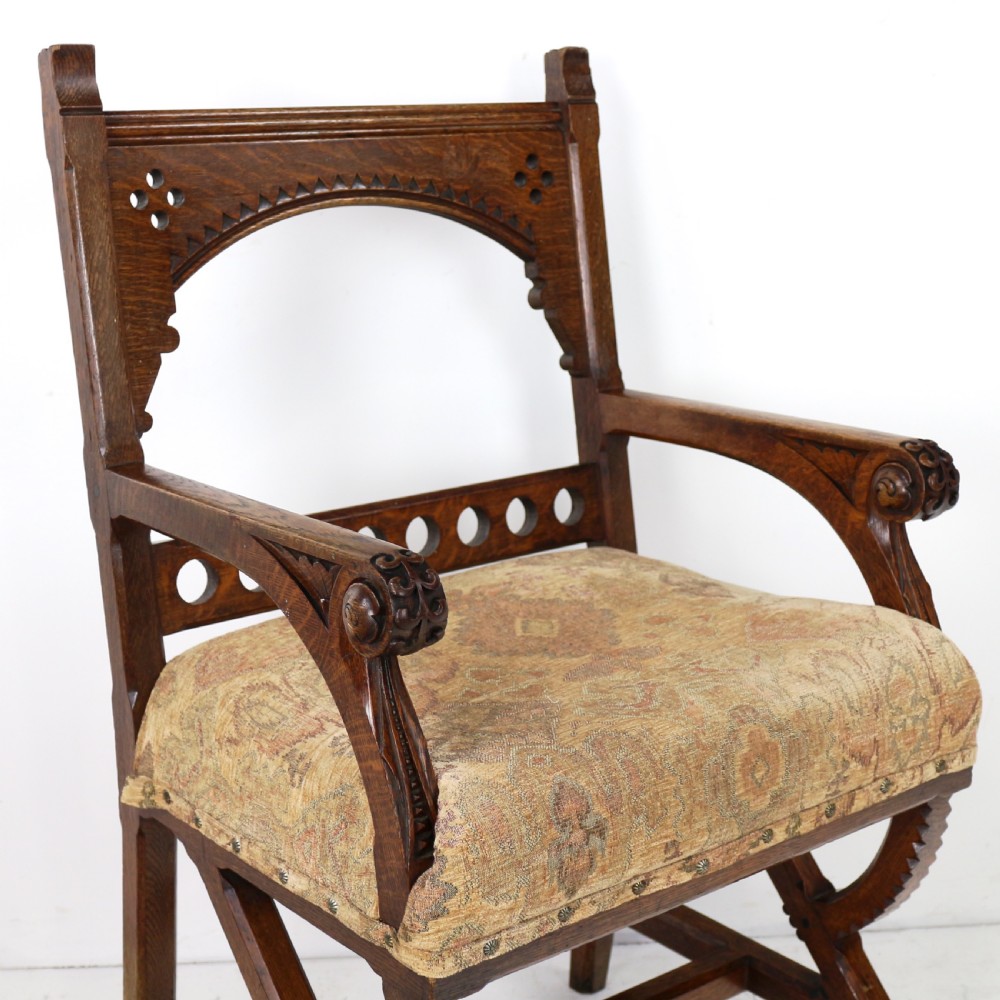 A Gothic Revival carved dark oak armchair featuring an arched backrest with quatrefoil cutouts, curved legs, and a patterned fabric seat. View VII