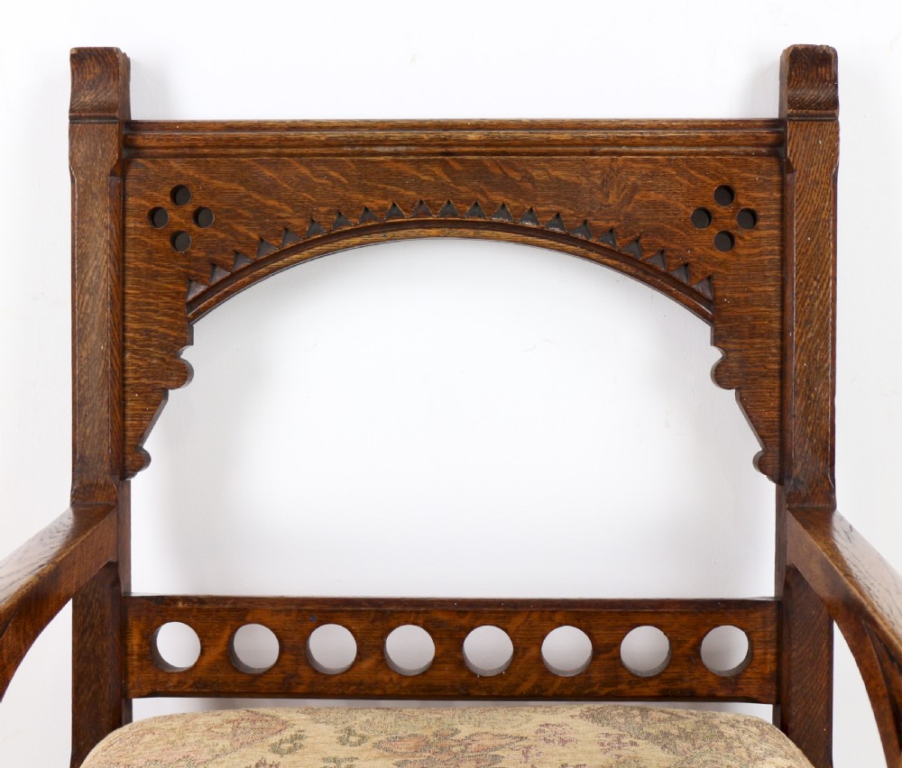 A Gothic Revival carved dark oak armchair featuring an arched backrest with quatrefoil cutouts, curved legs, and a patterned fabric seat. View IX
