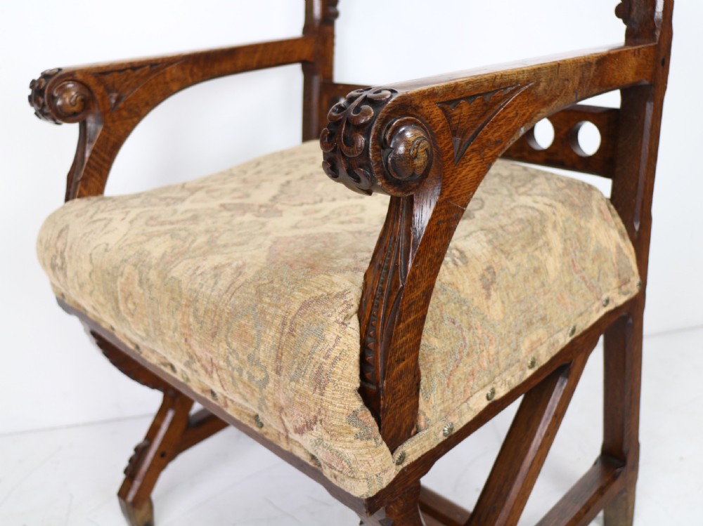 A Gothic Revival carved dark oak armchair featuring an arched backrest with quatrefoil cutouts, curved legs, and a patterned fabric seat. View XI