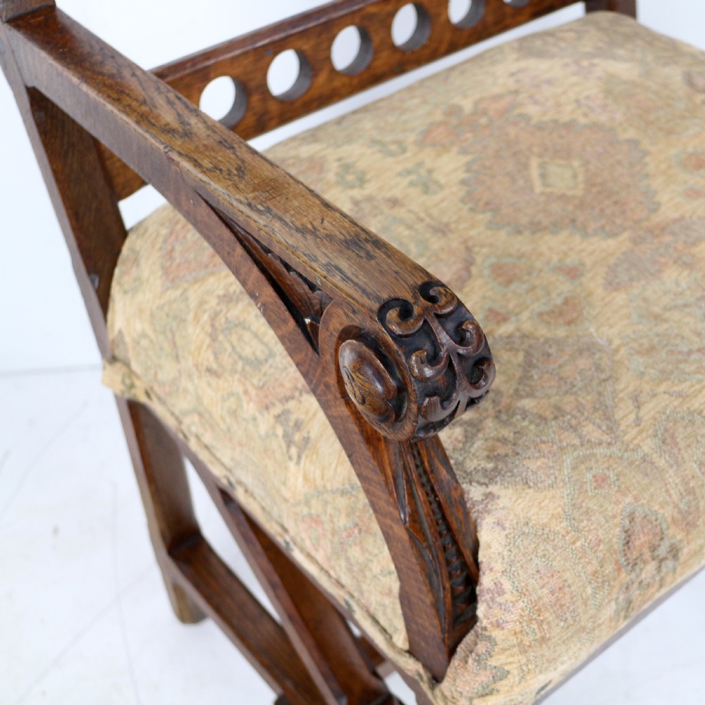 A Gothic Revival carved dark oak armchair featuring an arched backrest with quatrefoil cutouts, curved legs, and a patterned fabric seat. View XIII