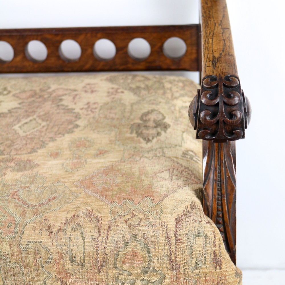 A Gothic Revival carved dark oak armchair featuring an arched backrest with quatrefoil cutouts, curved legs, and a patterned fabric seat. View XIV