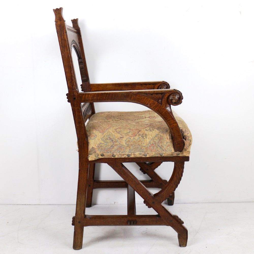 A Gothic Revival carved dark oak armchair featuring an arched backrest with quatrefoil cutouts, curved legs, and a patterned fabric seat. View XV