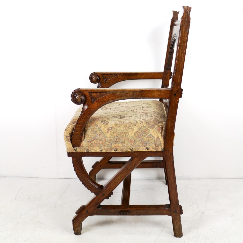 A Gothic Revival carved dark oak armchair featuring an arched backrest with quatrefoil cutouts, curved legs, and a patterned fabric seat. View XVI
