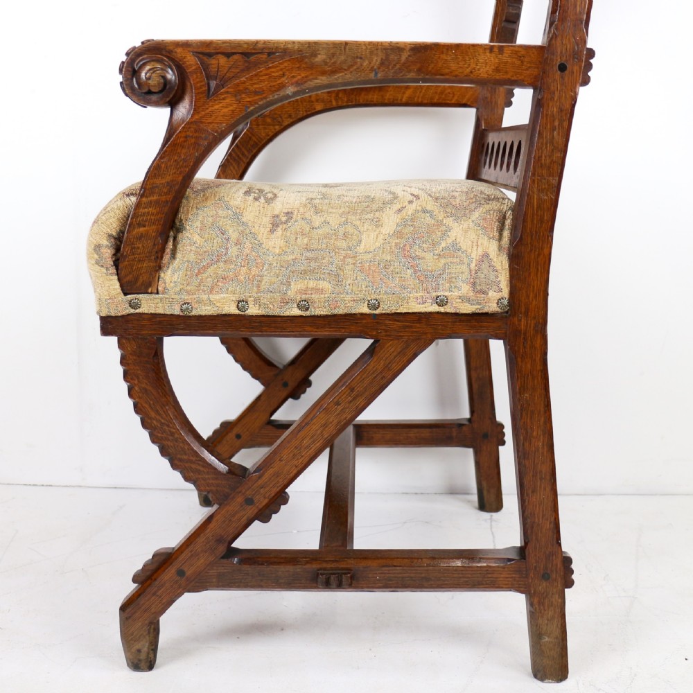 A Gothic Revival carved dark oak armchair featuring an arched backrest with quatrefoil cutouts, curved legs, and a patterned fabric seat. View XVIII
