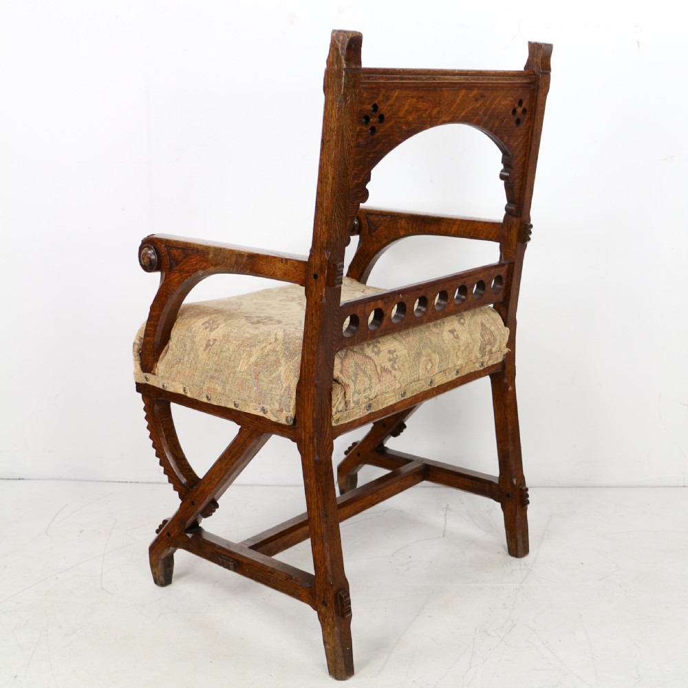 A Gothic Revival carved dark oak armchair featuring an arched backrest with quatrefoil cutouts, curved legs, and a patterned fabric seat. View XIX
