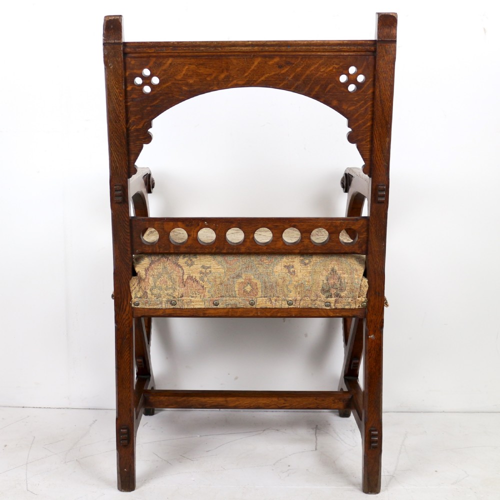 A Gothic Revival carved dark oak armchair featuring an arched backrest with quatrefoil cutouts, curved legs, and a patterned fabric seat. View XX