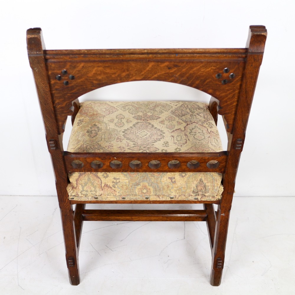A Gothic Revival carved dark oak armchair featuring an arched backrest with quatrefoil cutouts, curved legs, and a patterned fabric seat. View XXI