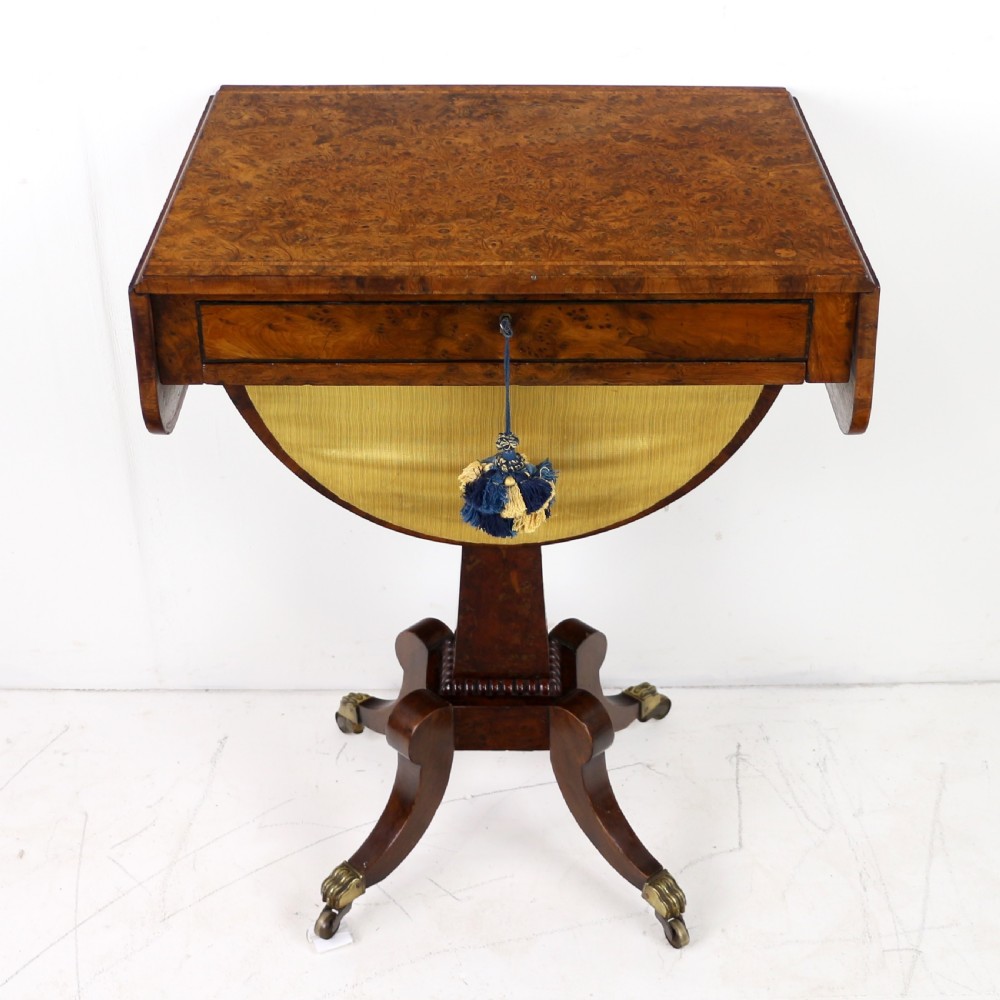 An Irish Regency drop-leaf work table featuring burr yew veneer, a single drawer, a yellow pleated fabric work well, and a quadruped pedestal base with brass castors. View II