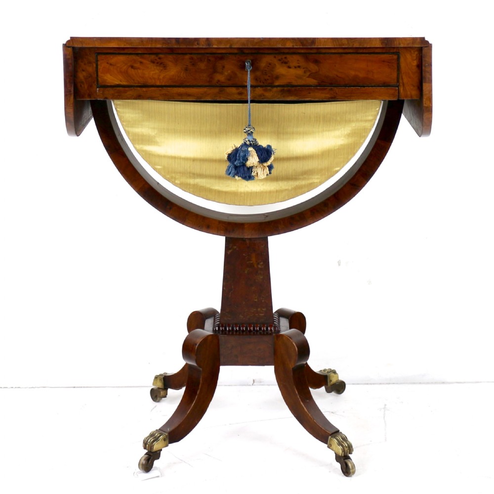 An Irish Regency drop-leaf work table featuring burr yew veneer, a single drawer, a yellow pleated fabric work well, and a quadruped pedestal base with brass castors. View III