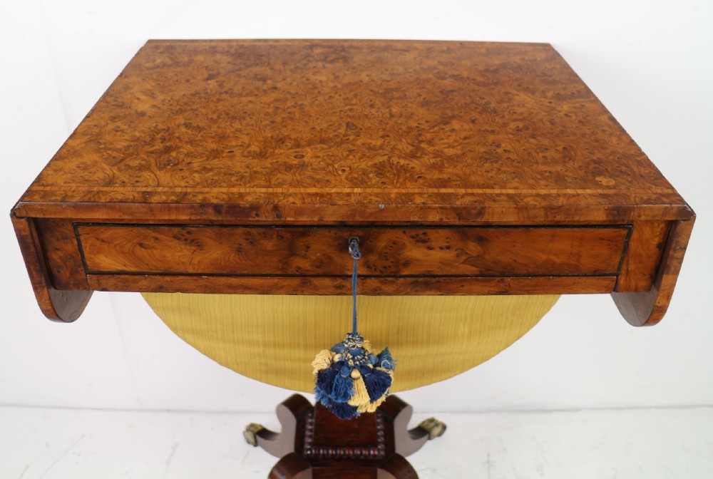 An Irish Regency drop-leaf work table featuring burr yew veneer, a single drawer, a yellow pleated fabric work well, and a quadruped pedestal base with brass castors. View VI