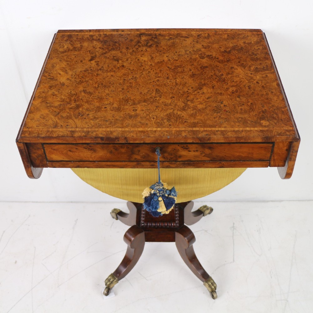 An Irish Regency drop-leaf work table featuring burr yew veneer, a single drawer, a yellow pleated fabric work well, and a quadruped pedestal base with brass castors. View VII
