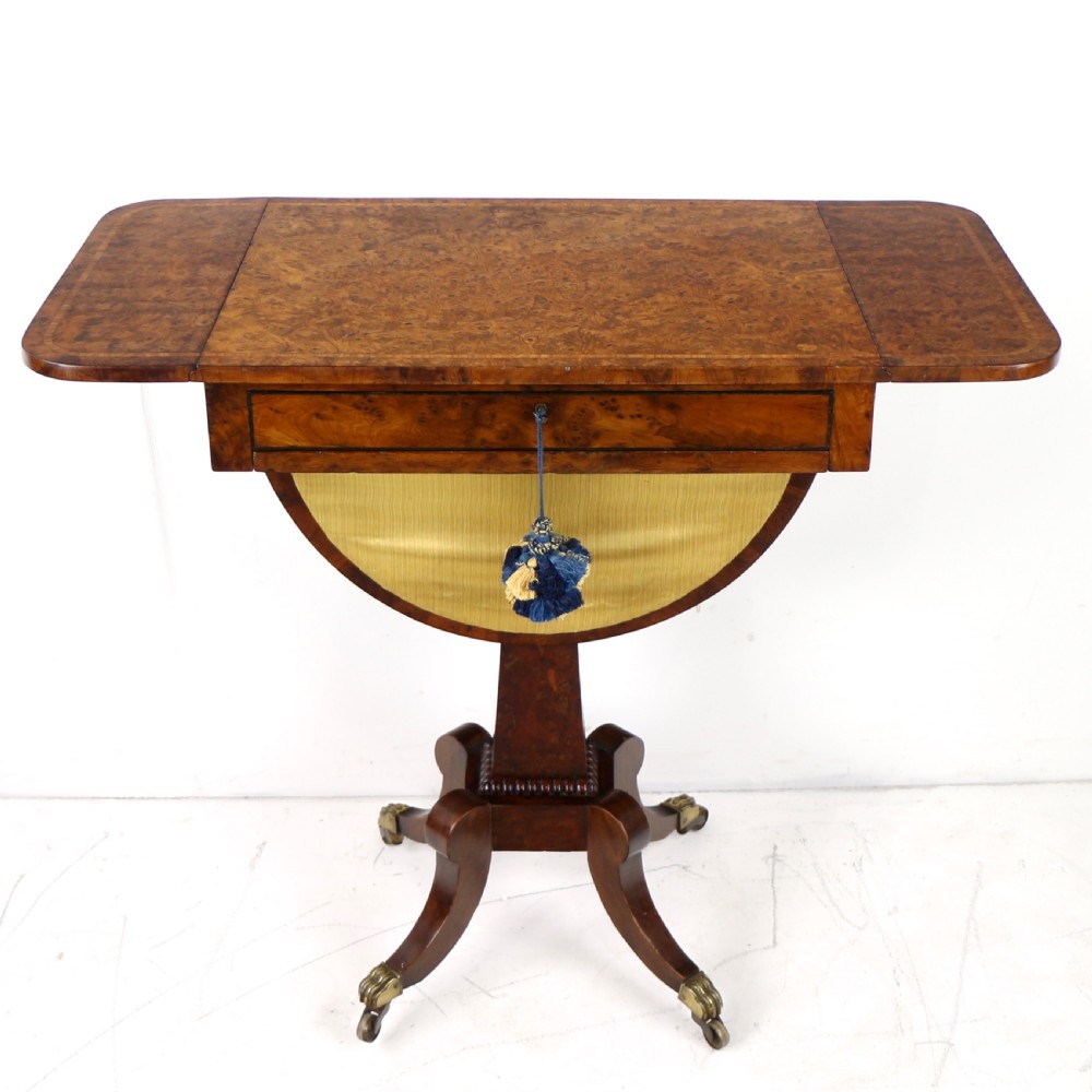 An Irish Regency drop-leaf work table featuring burr yew veneer, a single drawer, a yellow pleated fabric work well, and a quadruped pedestal base with brass castors. View VIII