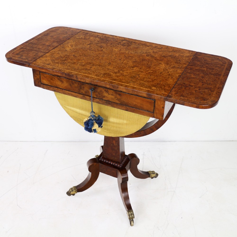 An Irish Regency drop-leaf work table featuring burr yew veneer, a single drawer, a yellow pleated fabric work well, and a quadruped pedestal base with brass castors. View IX