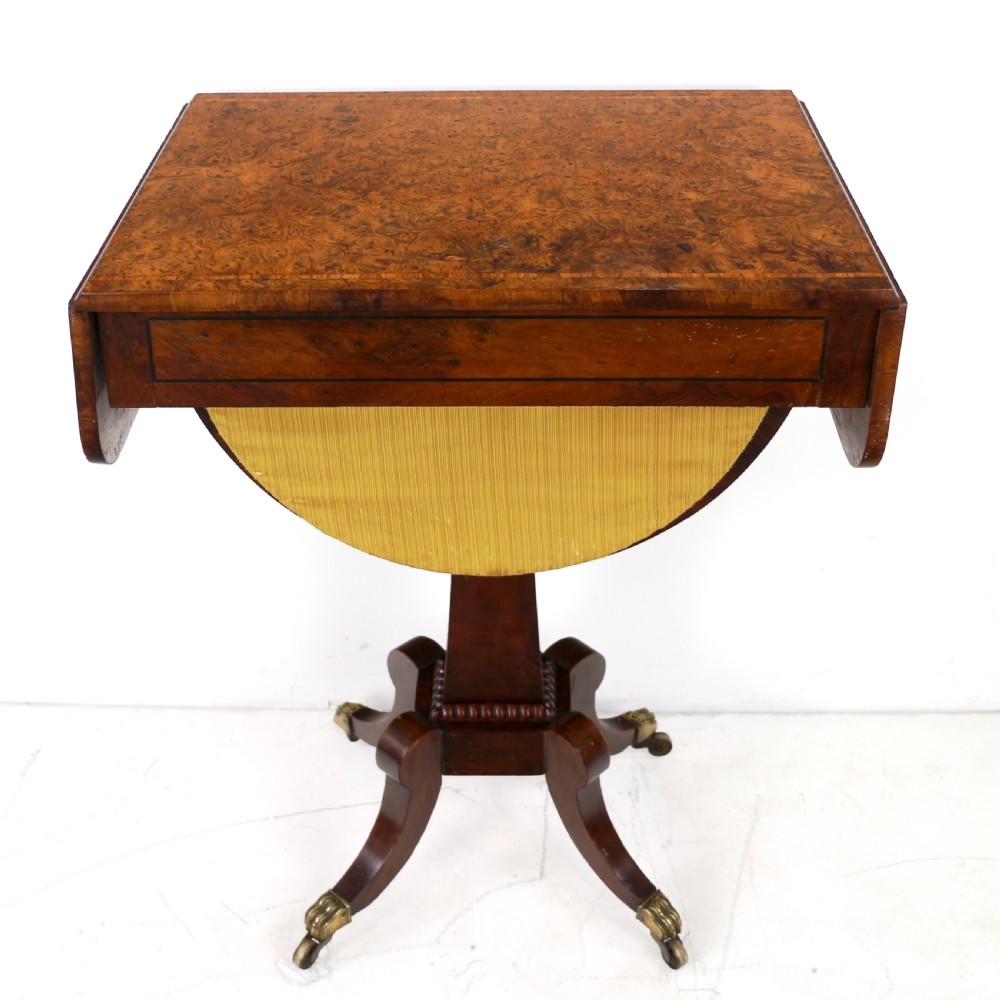 An Irish Regency drop-leaf work table featuring burr yew veneer, a single drawer, a yellow pleated fabric work well, and a quadruped pedestal base with brass castors. View XI