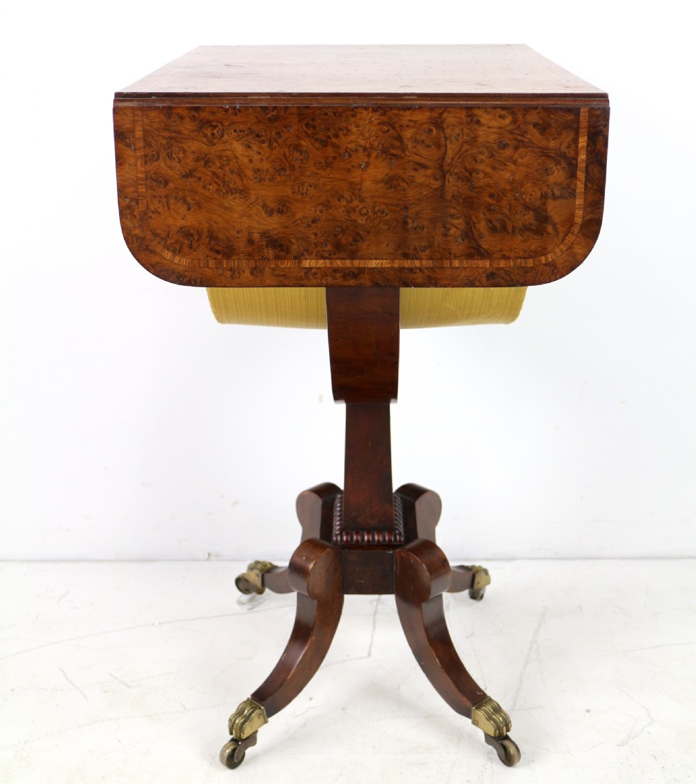 An Irish Regency drop-leaf work table featuring burr yew veneer, a single drawer, a yellow pleated fabric work well, and a quadruped pedestal base with brass castors. View XII