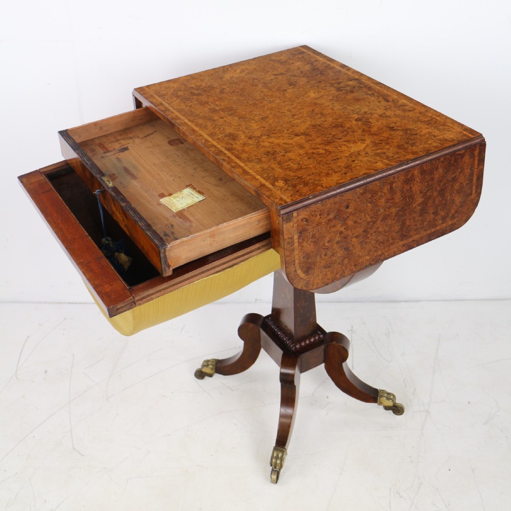 An Irish Regency drop-leaf work table featuring burr yew veneer, a single drawer, a yellow pleated fabric work well, and a quadruped pedestal base with brass castors. View XV