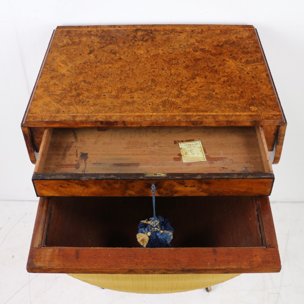 An Irish Regency drop-leaf work table featuring burr yew veneer, a single drawer, a yellow pleated fabric work well, and a quadruped pedestal base with brass castors. View XVI