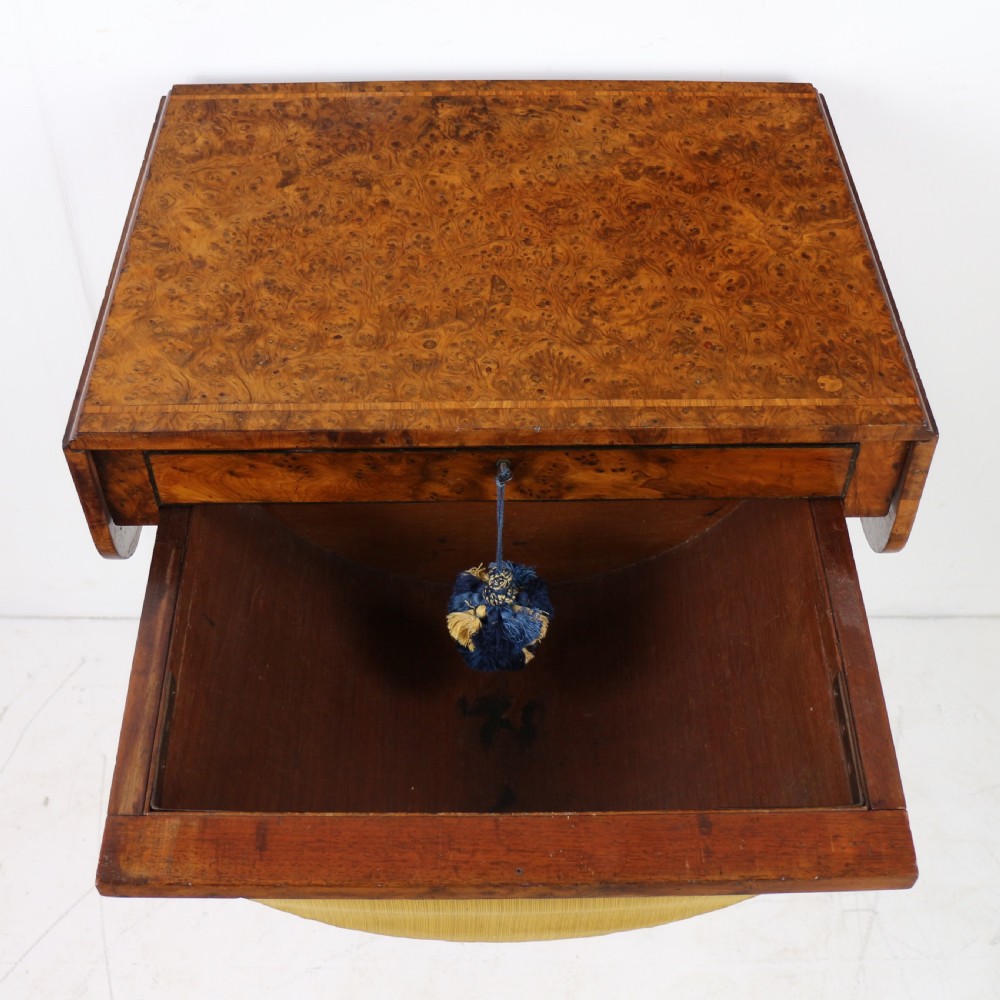 An Irish Regency drop-leaf work table featuring burr yew veneer, a single drawer, a yellow pleated fabric work well, and a quadruped pedestal base with brass castors. View XVIII