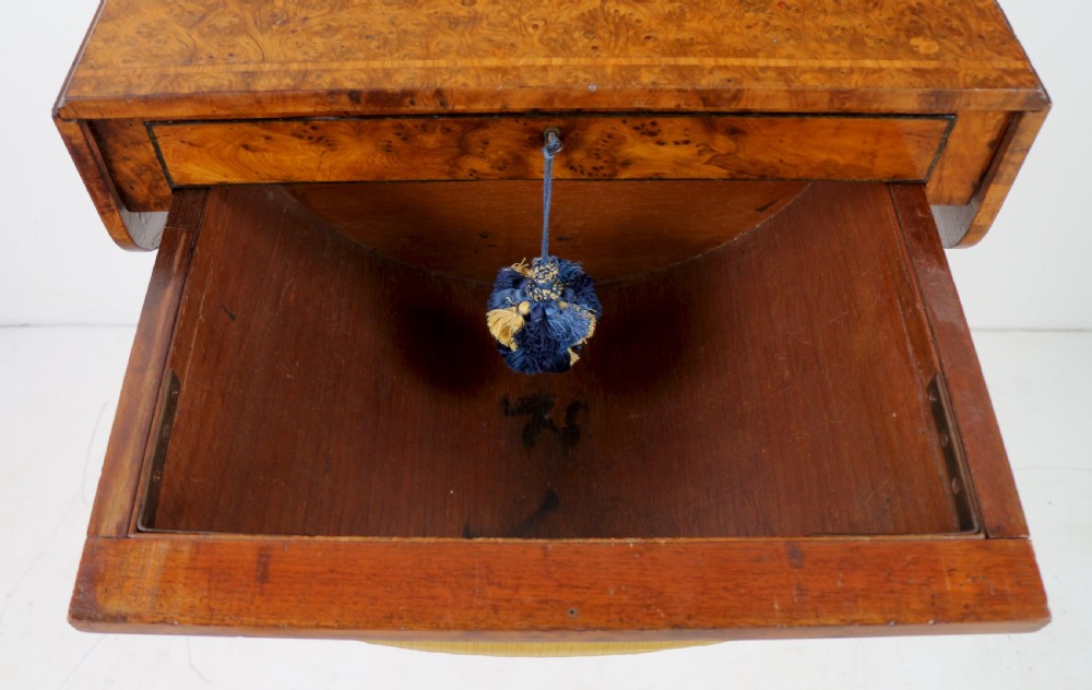 An Irish Regency drop-leaf work table featuring burr yew veneer, a single drawer, a yellow pleated fabric work well, and a quadruped pedestal base with brass castors. View XIX