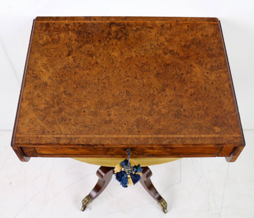 An Irish Regency drop-leaf work table featuring burr yew veneer, a single drawer, a yellow pleated fabric work well, and a quadruped pedestal base with brass castors. View XXI