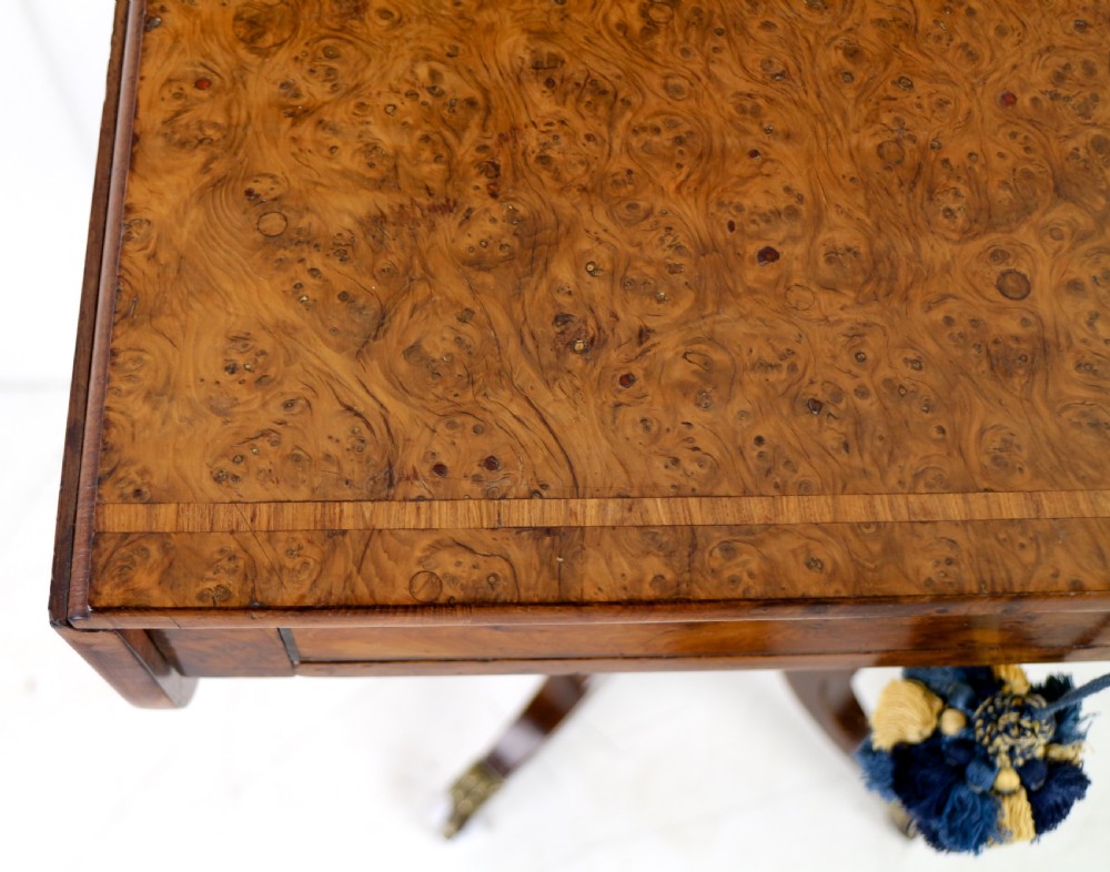 An Irish Regency drop-leaf work table featuring burr yew veneer, a single drawer, a yellow pleated fabric work well, and a quadruped pedestal base with brass castors. View XXII