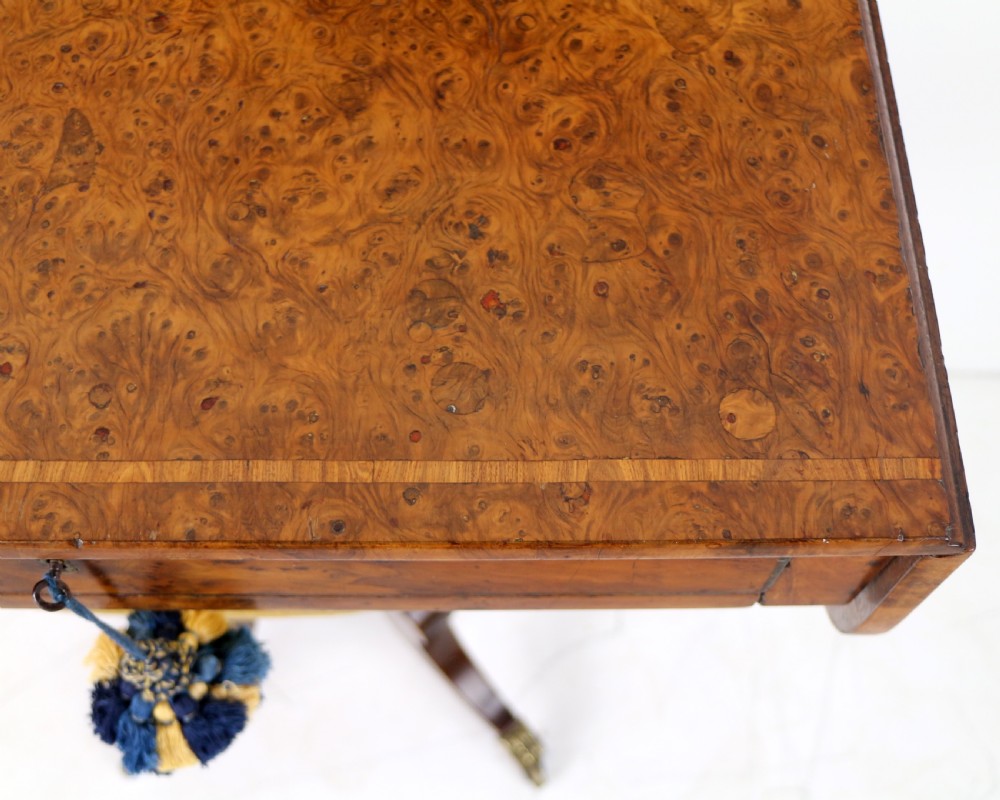 An Irish Regency drop-leaf work table featuring burr yew veneer, a single drawer, a yellow pleated fabric work well, and a quadruped pedestal base with brass castors. View XXIII
