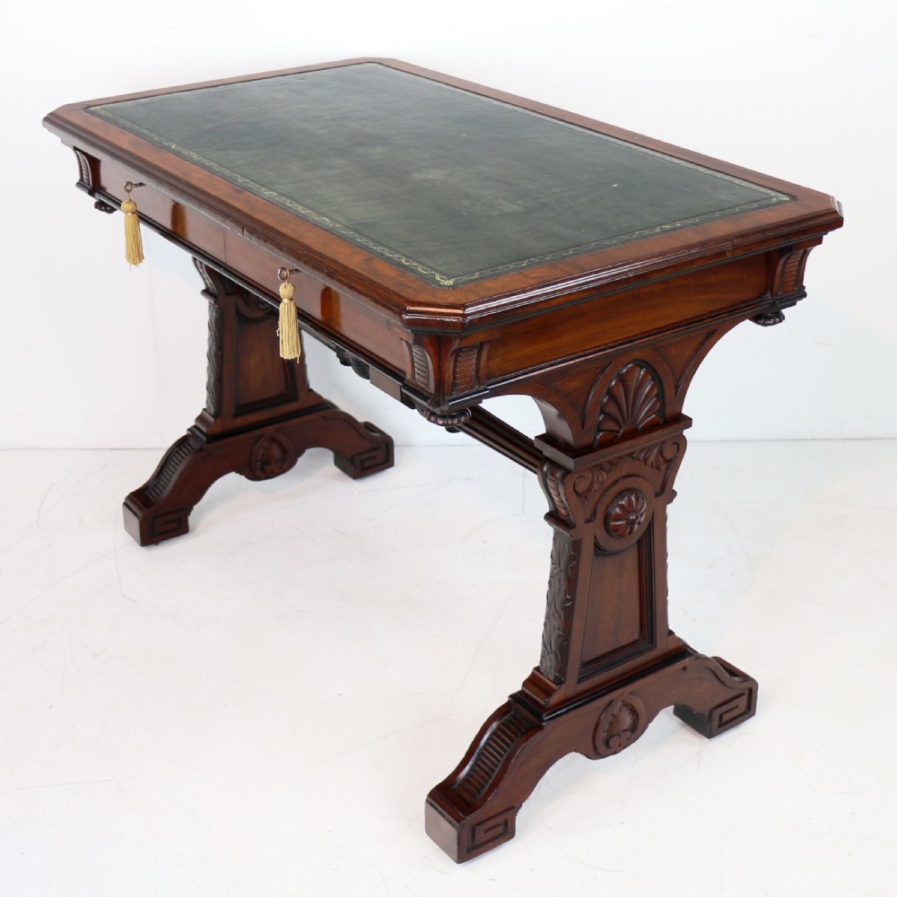 A Late Regency Neoclassical dark mahogany library table featuring a green leather inset writing surface, carved end supports with anthemion motifs, and frieze drawers with keys.