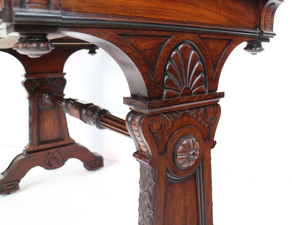 A Late Regency Neoclassical dark mahogany library table featuring a green leather inset writing surface, carved end supports with anthemion motifs, and frieze drawers with keys. View VI