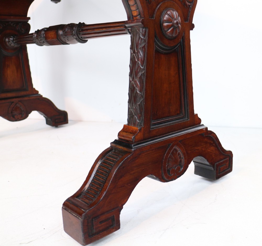 A Late Regency Neoclassical dark mahogany library table featuring a green leather inset writing surface, carved end supports with anthemion motifs, and frieze drawers with keys. View VII