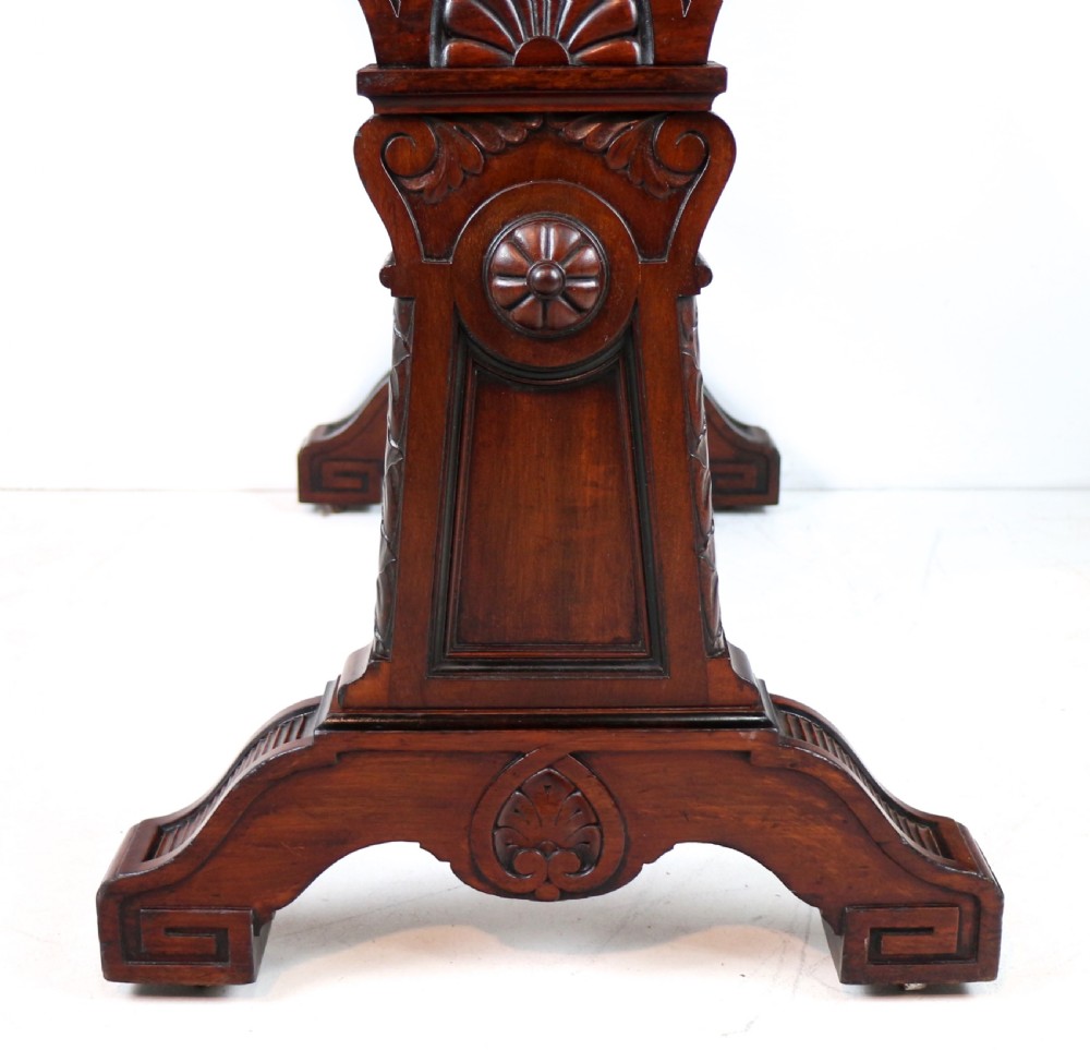 A Late Regency Neoclassical dark mahogany library table featuring a green leather inset writing surface, carved end supports with anthemion motifs, and frieze drawers with keys. View IX