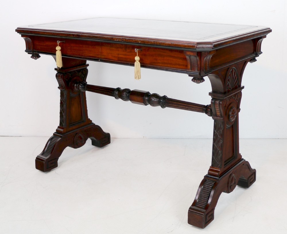 A Late Regency Neoclassical dark mahogany library table featuring a green leather inset writing surface, carved end supports with anthemion motifs, and frieze drawers with keys. View X