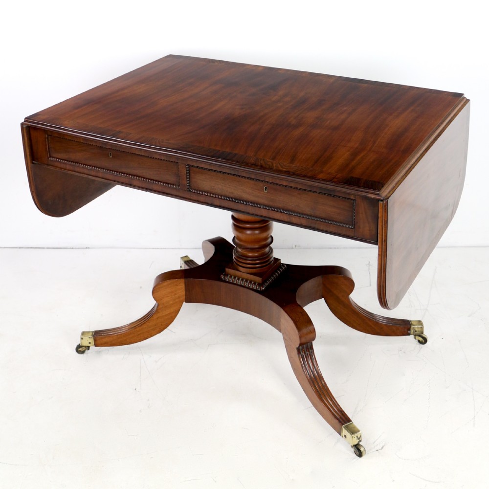 A Regency mahogany drop-leaf sofa table with frieze drawers, turned pedestal, reeded quadrupod legs, and brass castors.