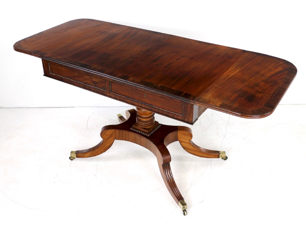 A Regency mahogany drop-leaf sofa table with frieze drawers, turned pedestal, reeded quadrupod legs, and brass castors. View II